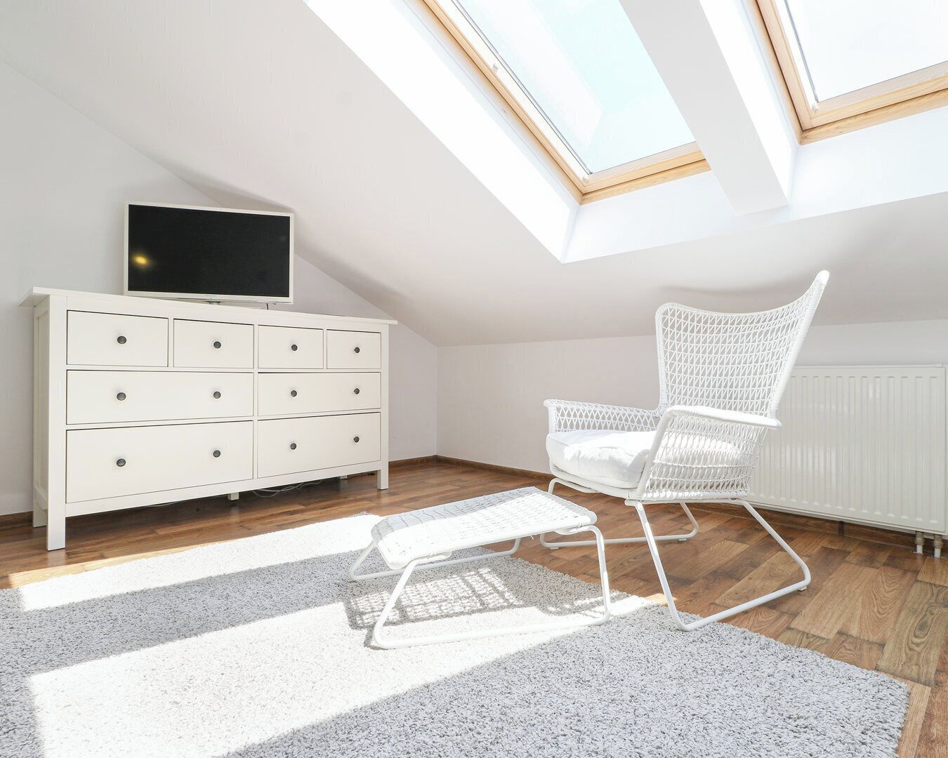 A room with a white dresser, a white rocking chair, and a skylight.