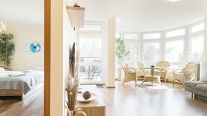 A spacious living room with a wooden floor, a dining area with wicker chairs, and large windows providing natural light. - Villa Mistral by Baltic Home (Swinoujscie)