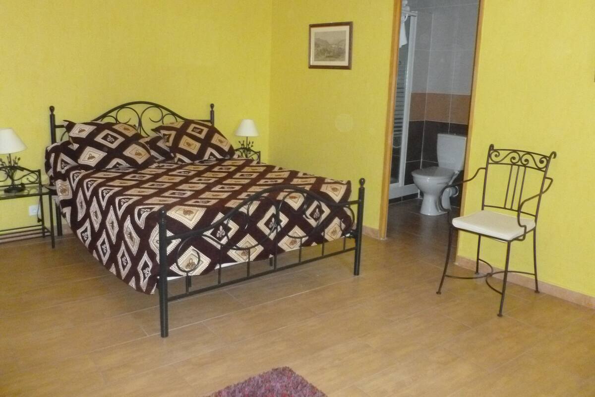 Une chambre à coucher comprenant un lit, des lampes de chevet, une chaise et une porte donnant sur une salle de bain.