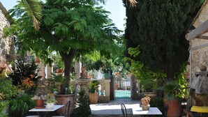 Une terrasse extérieure avec des tables et des chaises, entourée de plantes en pot et d’un mur de pierre.