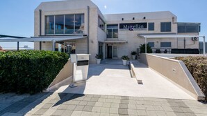 Ein modernes Gebäude mit Café-Bar und Restaurant namens Magellan. Es hat ein flaches Dach, große Fenster und eine gepflasterte Eingangszone.