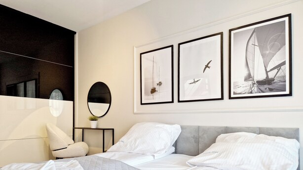 A hotel room with a bed, a bedside table with a mirror, and three framed pictures on the wall. - Holiday House by Baltic Home (Swinoujscie)