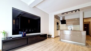 A modern living room with a large flat-screen TV, a dark wooden entertainment unit, and a glass kitchen island. - Holiday House by Baltic Home (Swinoujscie)