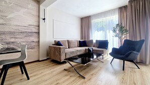A modern living room with a sofa, armchair, coffee table, and a dining area with a chair and table. - Holiday House by Baltic Home (Swinoujscie)