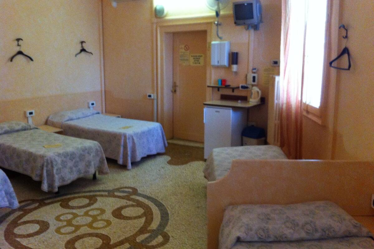 A hotel room with two single beds, a small kitchenette, a desk, and a TV.