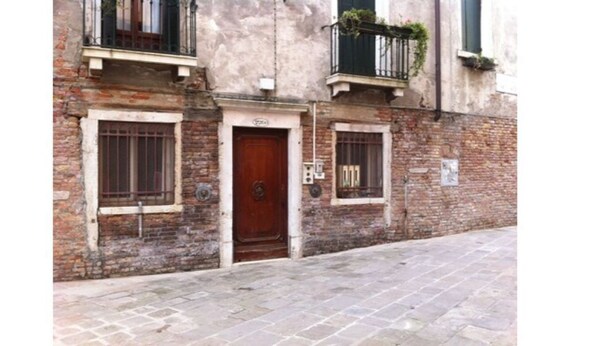 A narrow street with a building featuring a wooden door and barred windows. - Cadoro (Venice)