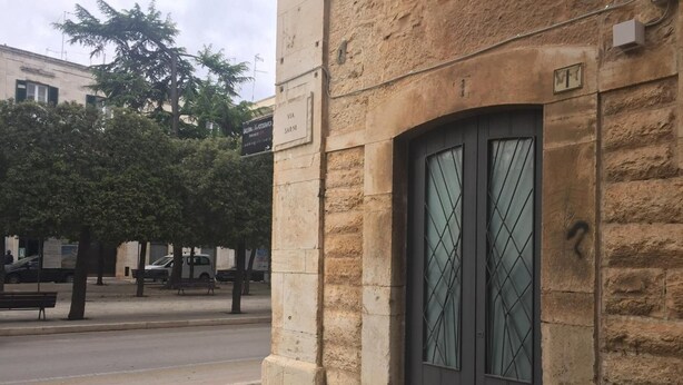 A stone building with a dark arched entrance and a large flower planter in front. - B&B Casa Catalano (Terlizzi)
