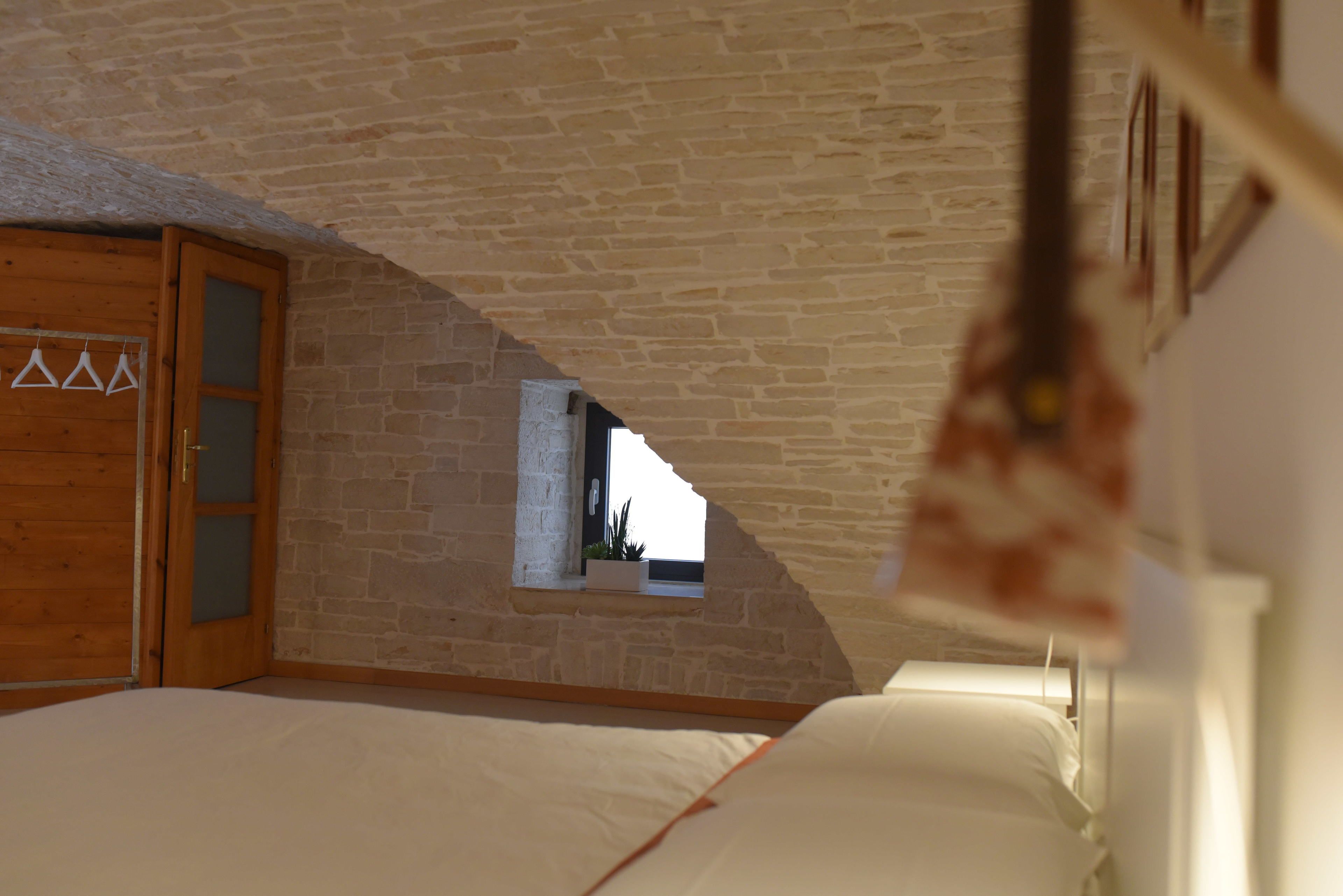 A bedroom with a sloped ceiling, a wooden door, a small window, and a bed with white bedding.