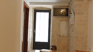 A room with a tiled floor, a glass table with a decorative item, a wooden chair, a black-framed door, and a stone wall with a mounted TV. - B&B L' alcova (Terlizzi)