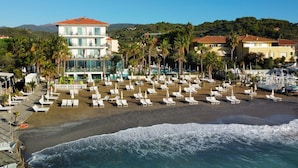 A beach resort with multiple lounge chairs and umbrellas, a pool area, and a view of the ocean. - Hotel Caravelle Thalasso & Wellness (Diano Marina)