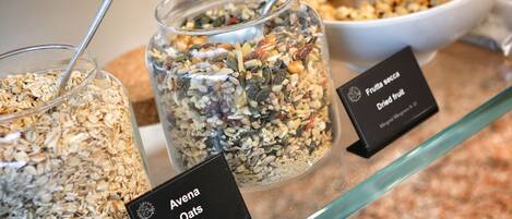 Three labeled containers of granola on a glass shelf.
