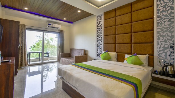 A hotel room with a large bed, a wooden ceiling, a sofa, and a view of the outdoors. - Treebo Prince Palace With Swimming Pool (Mahabaleshwar)
