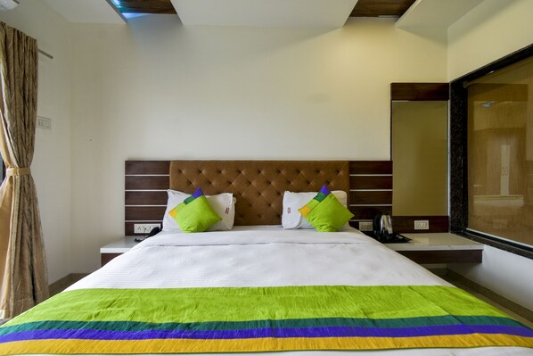 Une chambre d’hôtel avec un grand lit, une tête de lit en bois, deux oreillers verts, une couvre-lit blanche et un miroir au mur.