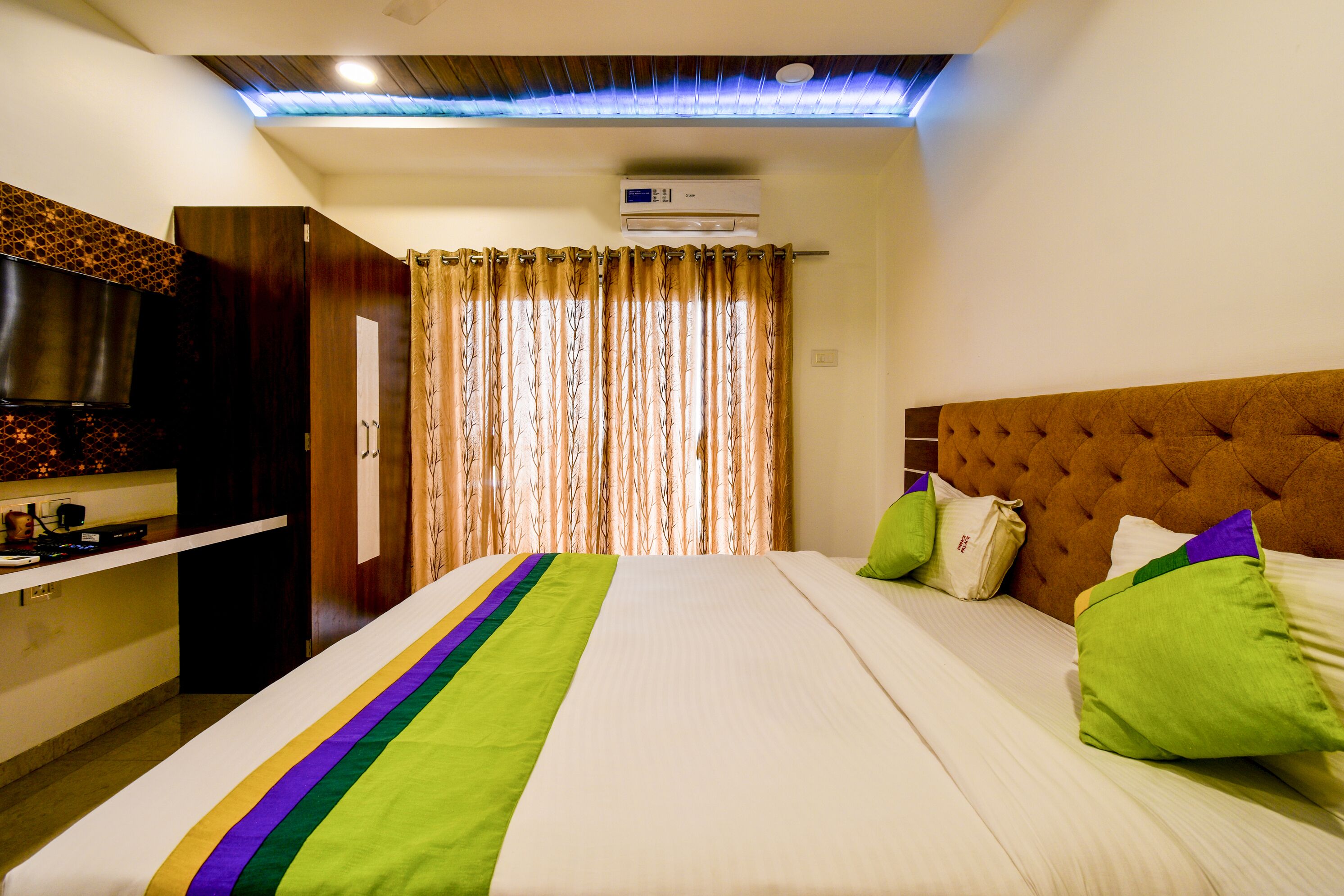 A hotel room with a bed, a TV, a wardrobe, and an air conditioning unit.