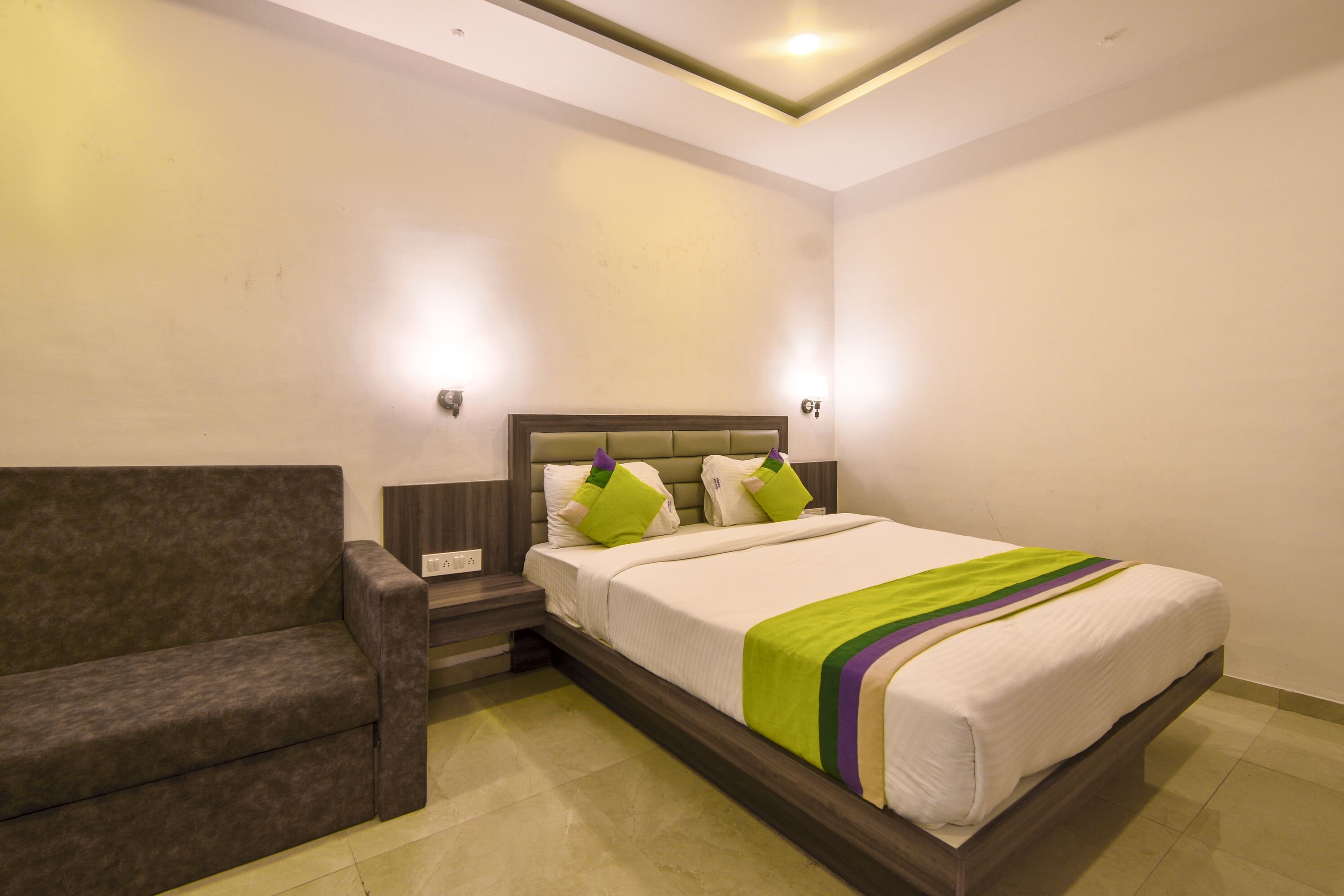 A bedroom with a bed, a nightstand, a sofa, and a wall-mounted light fixture.