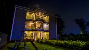A multi-story building with a balcony on the second floor, a slide in the yard, and a well-lit entrance. - Treebo Prince Palace With Swimming Pool (Mahabaleshwar)