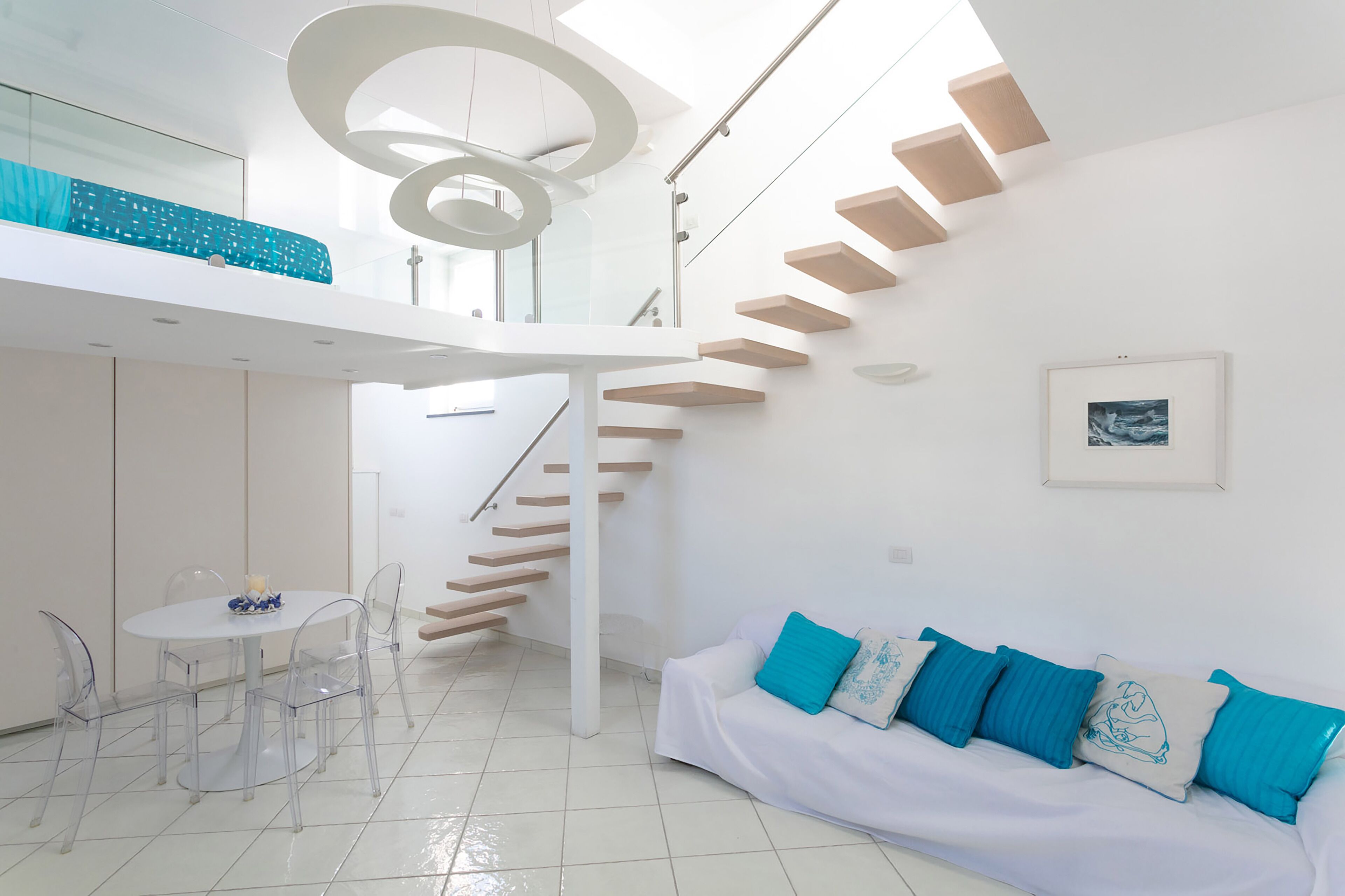 A modern interior with a staircase, a dining area, and a sofa with blue cushions.