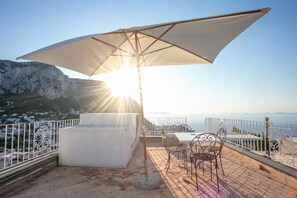 Une terrasse avec une table et des chaises, un grand parasol, et une vue sur une ville côtière et des falaises.