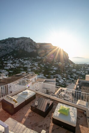 Une terrasse sur le toit, dotée d’un espace extérieur aménagé avec des sièges, une rambarde et offrant une vue sur une ville côtière et des montagnes.