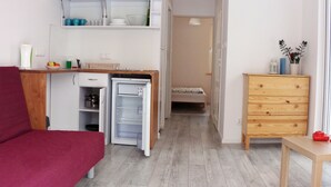 Quarto compacto com cozinha compacta, uma cama, cómoda de madeira e sofá vermelho.