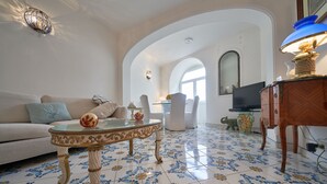 Una sala de estar con sofá, una mesa de centro de vidrio, televisor y lámpara.