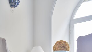 Una habitación con una silla blanca, una mesa de vidrio con un cuenco de flores y una lámpara.