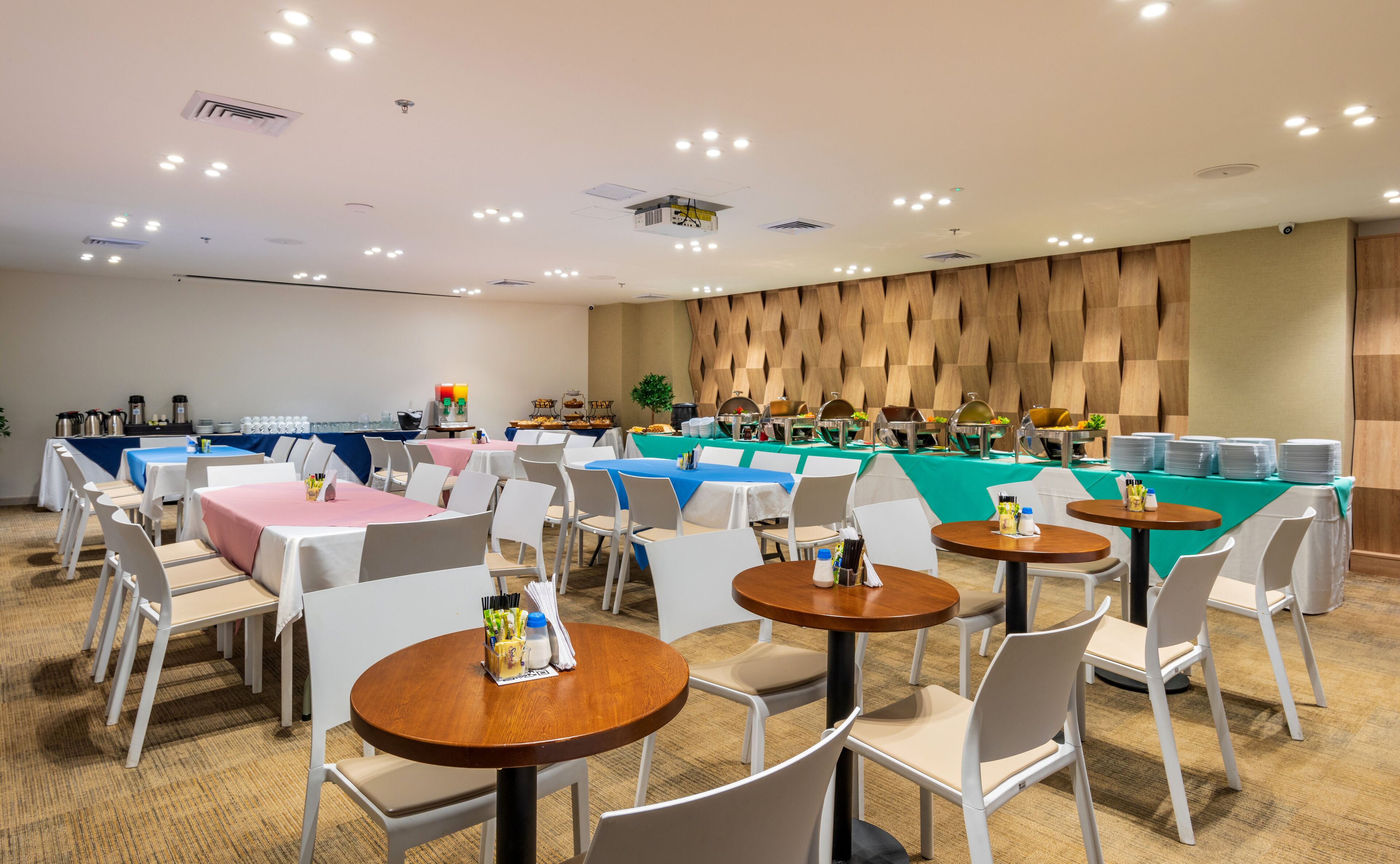 A conference room with multiple tables and chairs, equipped with a projector and air conditioning.