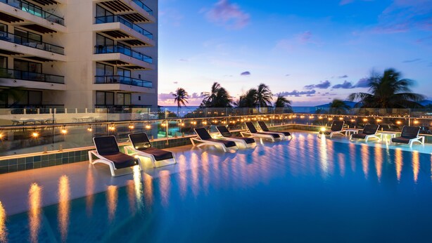 A poolside area with lounge chairs and a building with balconies. - Samawi (San Andrés)
