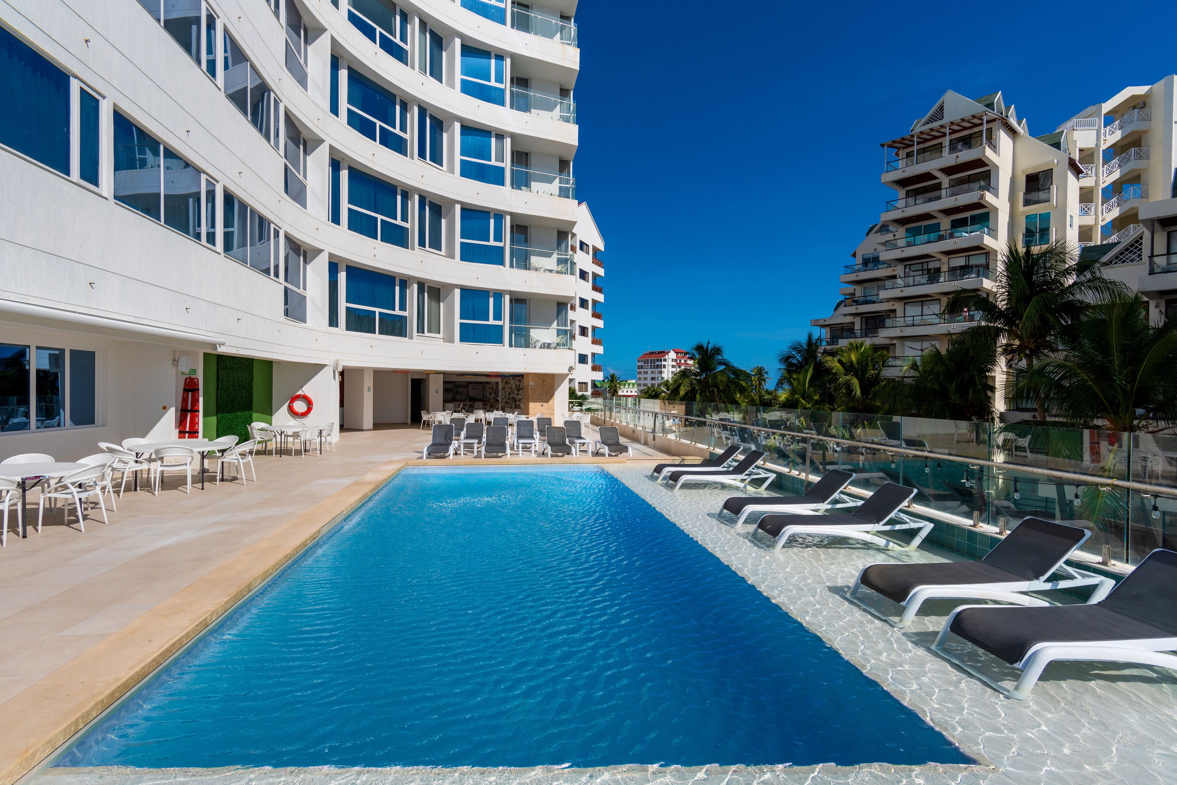 A swimming pool with lounge chairs and a building with multiple balconies.