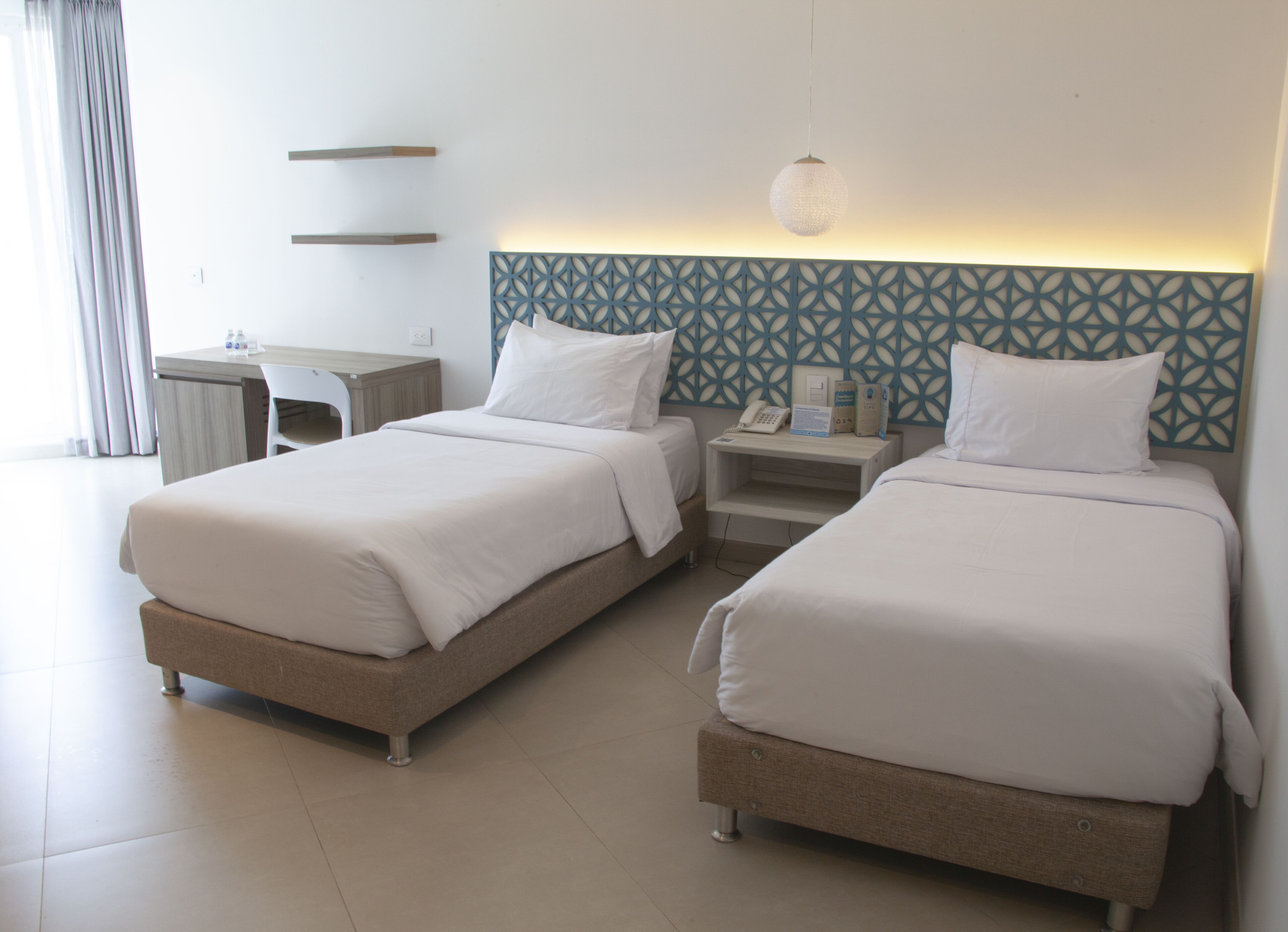 A hotel room with two beds, a desk, and a patterned headboard.