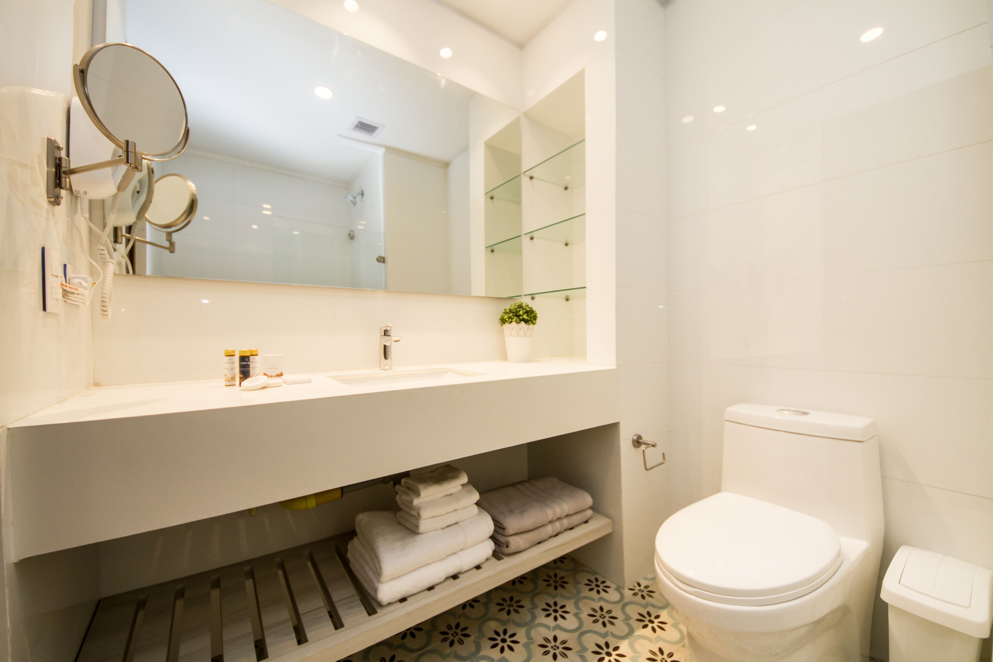 A modern bathroom with a white sink, a large mirror, a toilet, and a shelf with folded towels.