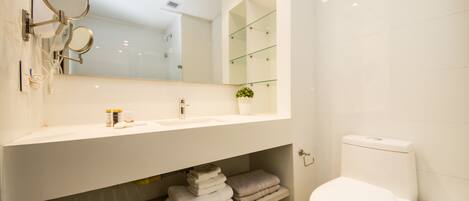 A modern bathroom with a white sink, a large mirror, a toilet, and a shelf with folded towels.