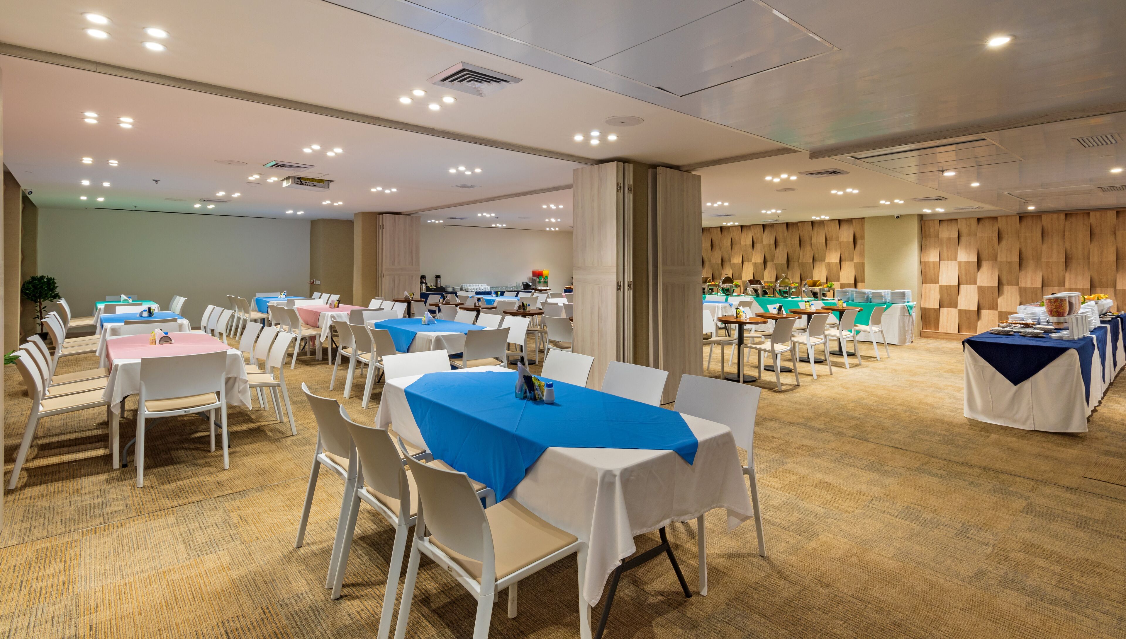 Une salle de conférence dotée de plusieurs tables et chaises, équipée de luminaires au plafond et d’un mur décoratif en bois.
