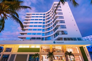 Un hotel moderno con fachada curva, varios balcones y una entrada bien iluminada.