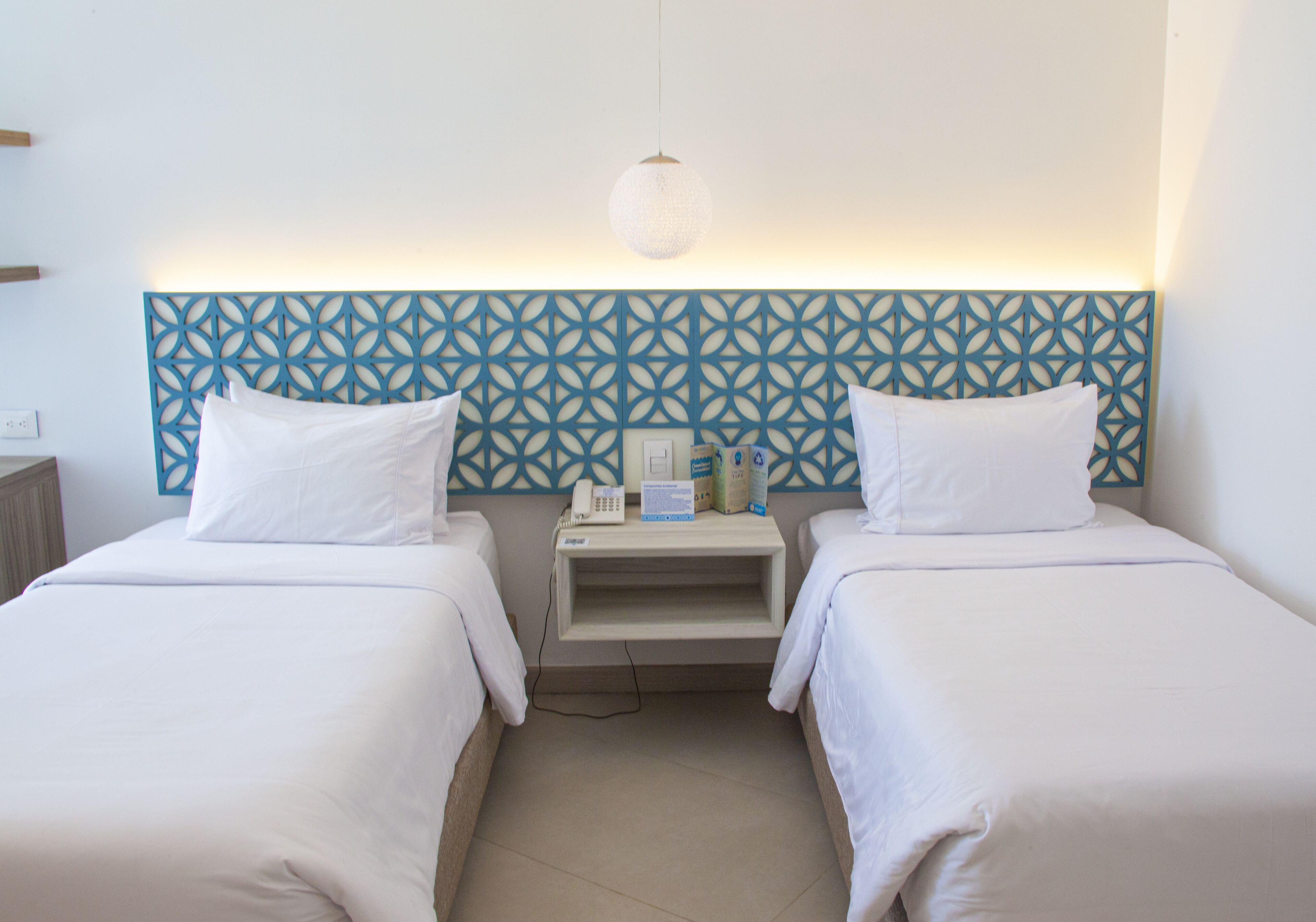 A hotel room with two single beds, a nightstand with a phone and a box, and a decorative blue headboard.