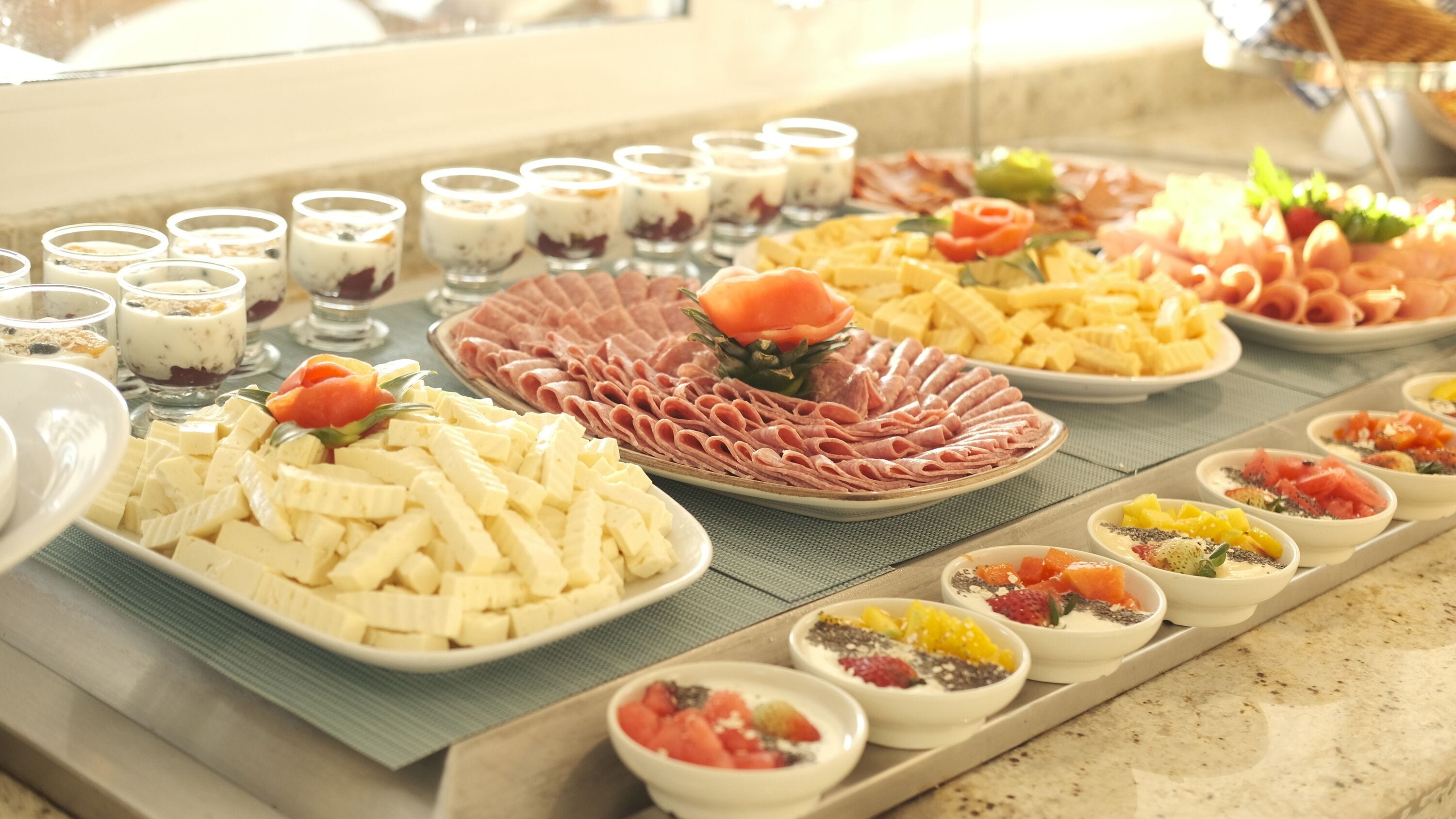 Buffet com diversos pratos, incluindo queijo, presunto e frutas.