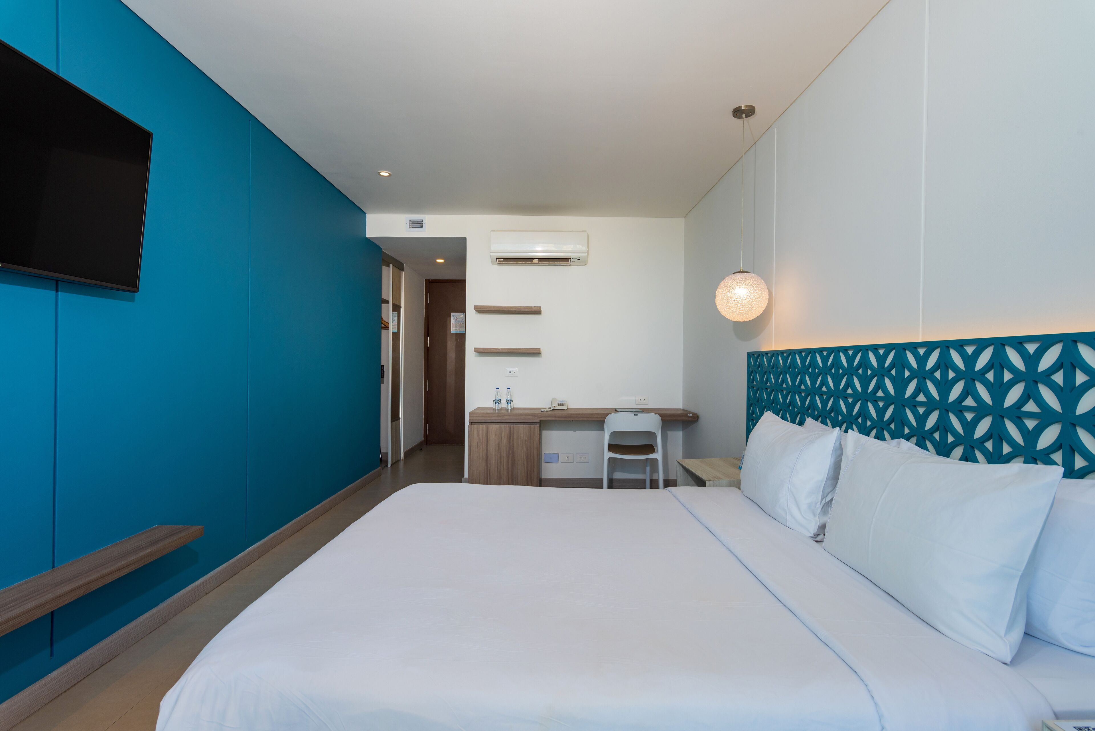 A hotel room with a bed, a desk, a chair, and a TV mounted on the wall.