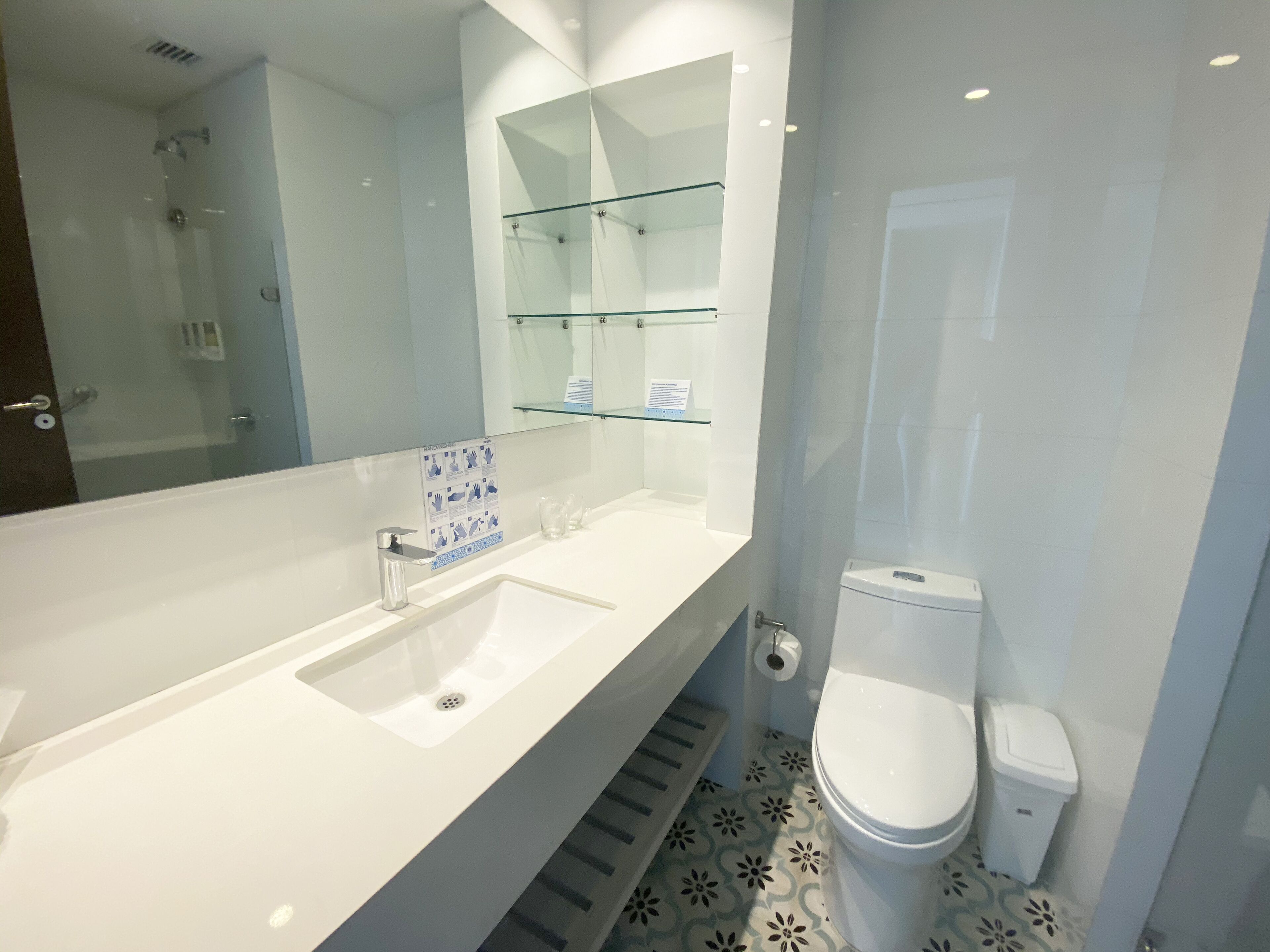 A modern bathroom with a large mirror, a white sink, and a toilet.