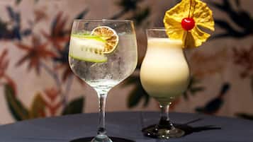 Dois cocktails sobre uma mesa, com papel de parede de tema tropical.