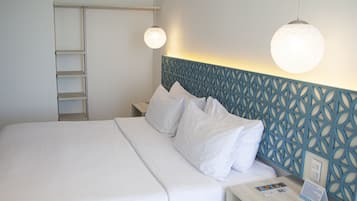 Una cama bien hecha con sábanas blancas, cabecera con estampado geométrico y mesita de noche con lámpara y folletos informativos.