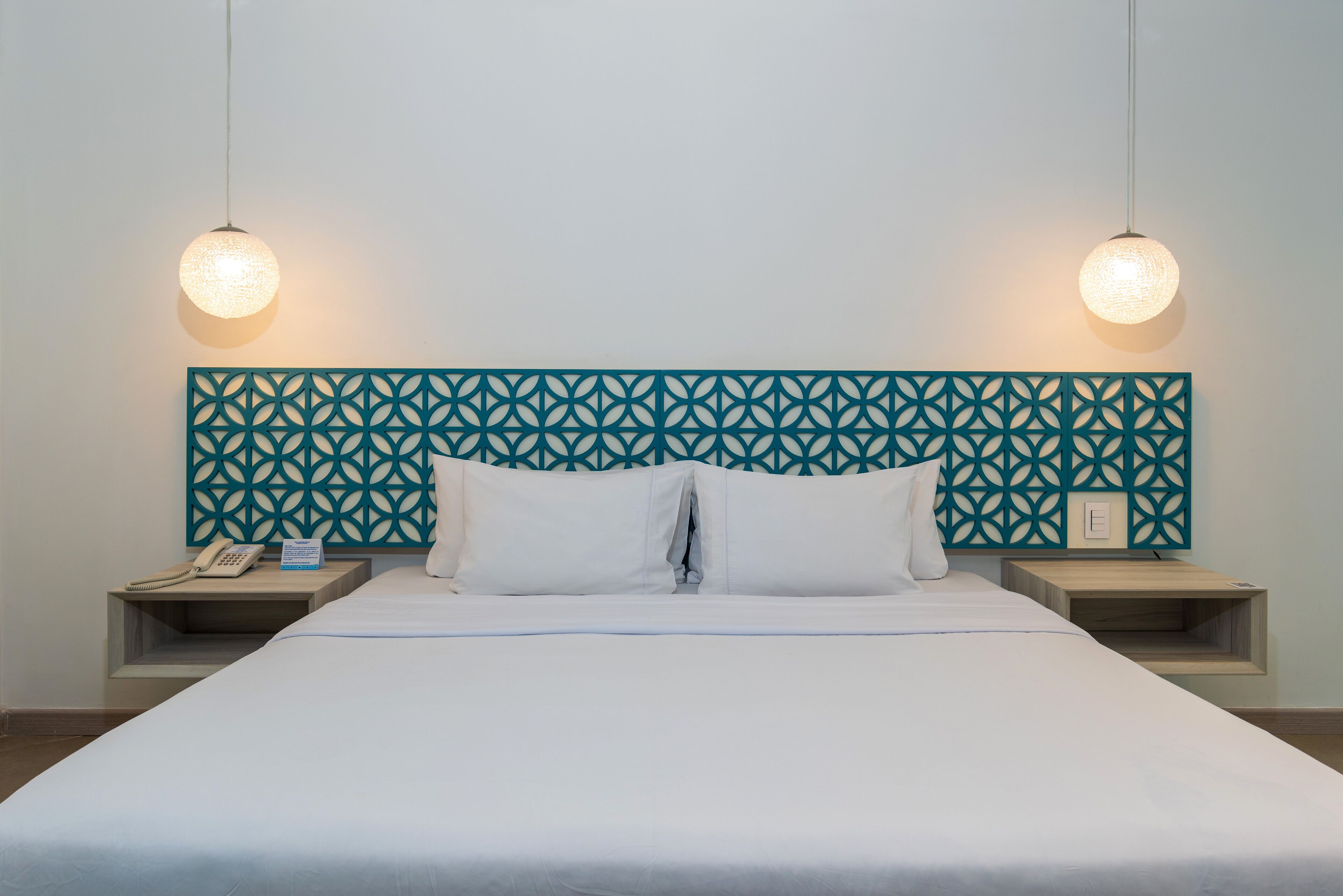 Ett hotellrum med en säng, två sängbord, en dekorativ sänggavel och två hängande taklampor.