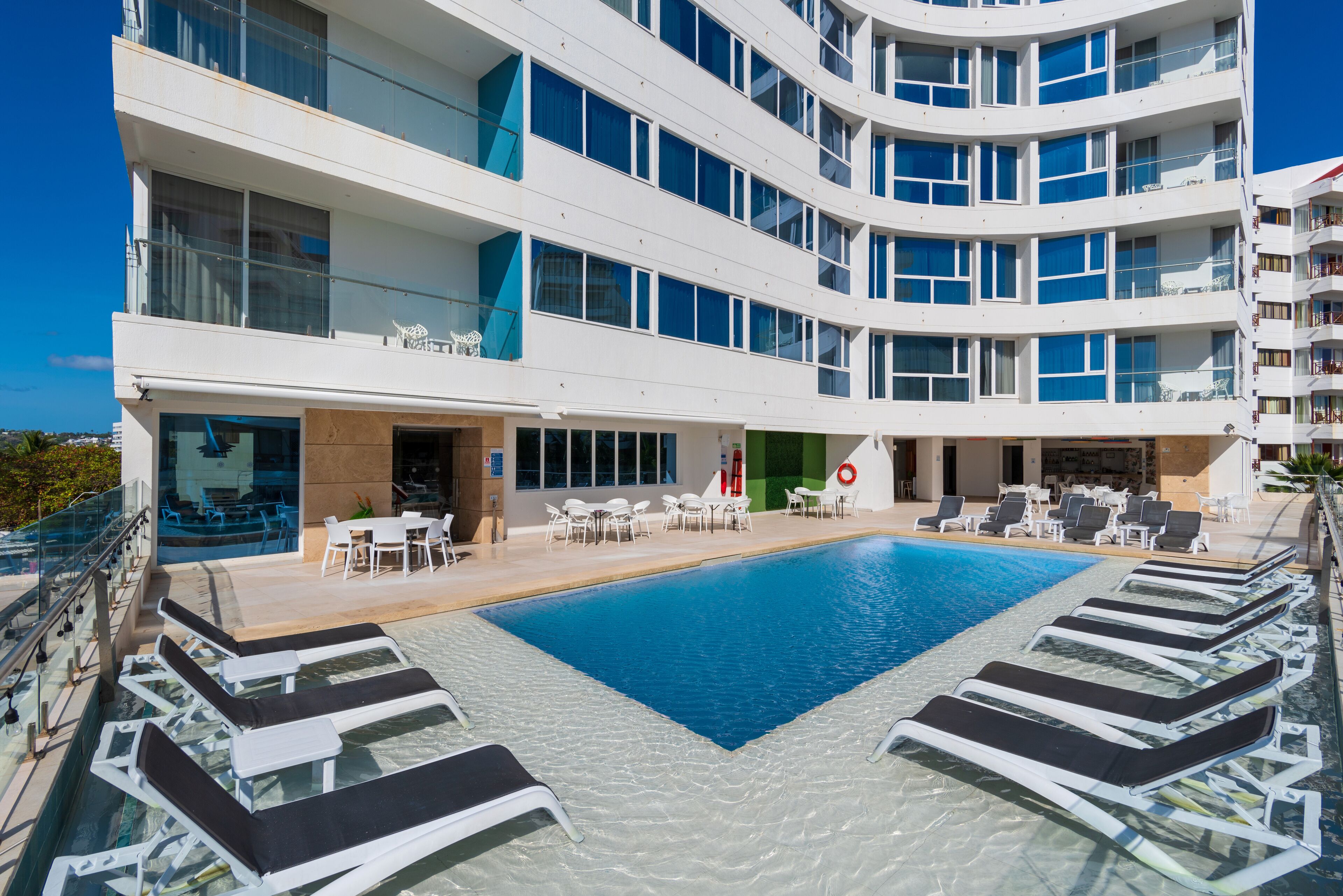 A modern hotel with a rooftop pool, outdoor seating, and multiple balconies.