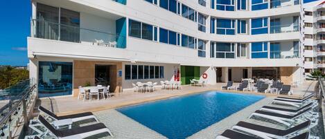 A modern hotel with a rooftop pool, outdoor seating, and multiple balconies.