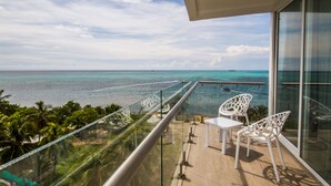 A balcony with a glass railing overlooking a turquoise sea, white chairs, and a small table. - Samawi (San Andrés)