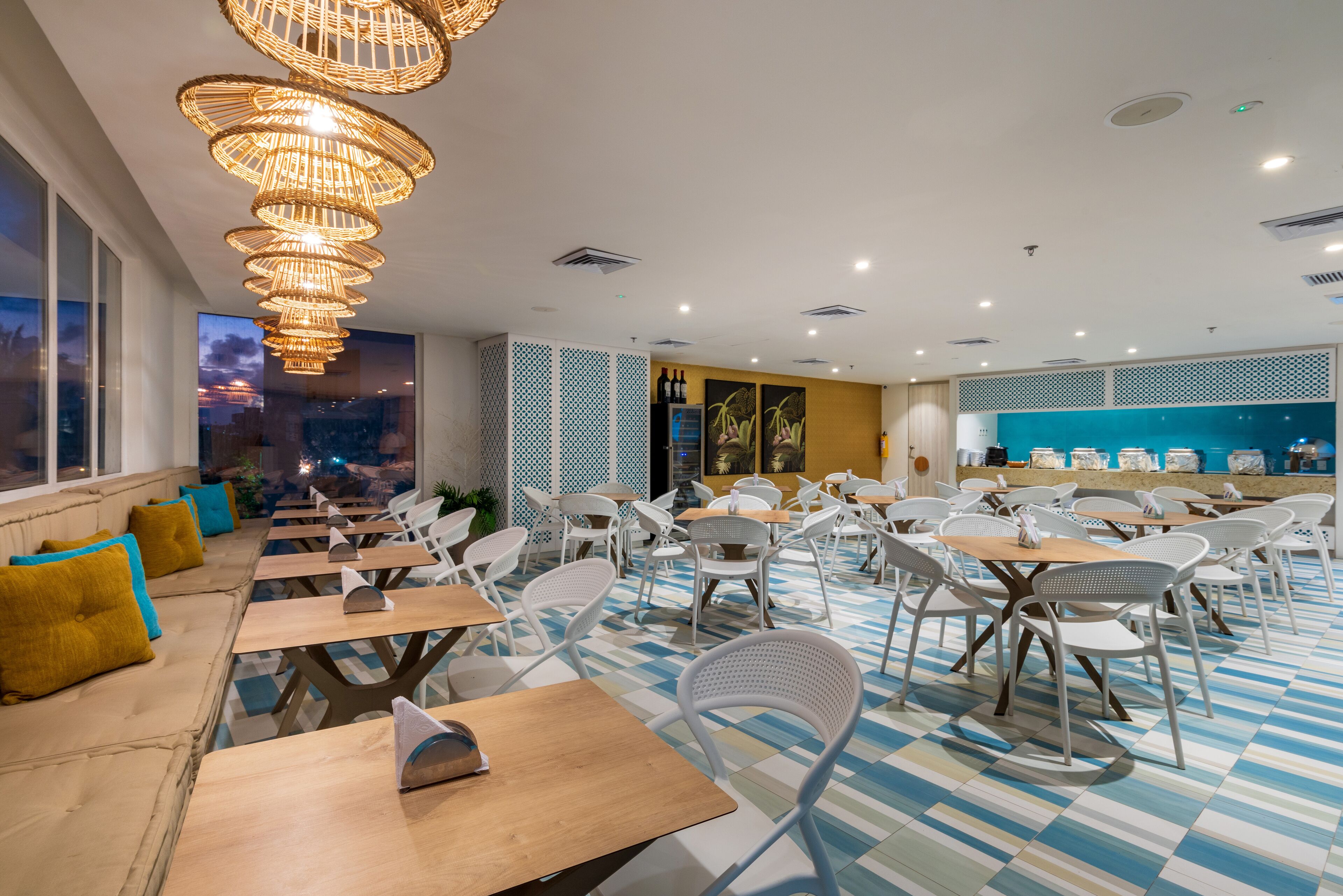 Un restaurante con varias mesas y sillas, un suelo con estampado y vistas a la ciudad a través de grandes ventanales.