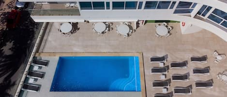 An aerial view of a hotel with a swimming pool, sun loungers, and outdoor seating areas.