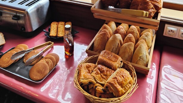Una vitrina de panadería con varios productos horneados, un tostador y vista a la calle desde una ventana.