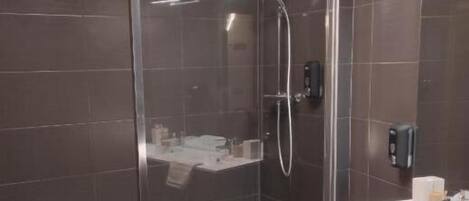 A modern bathroom with a glass-enclosed shower, a white sink, and dark tiled walls.