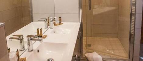 Um banheiro moderno com duas pias, box de vidro para o chuveiro e uma toalha no chão.