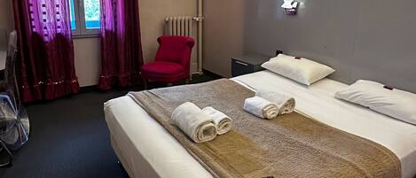 Habitación de hotel con una cama grande, una silla roja, un radiador y un cuadro en la pared.